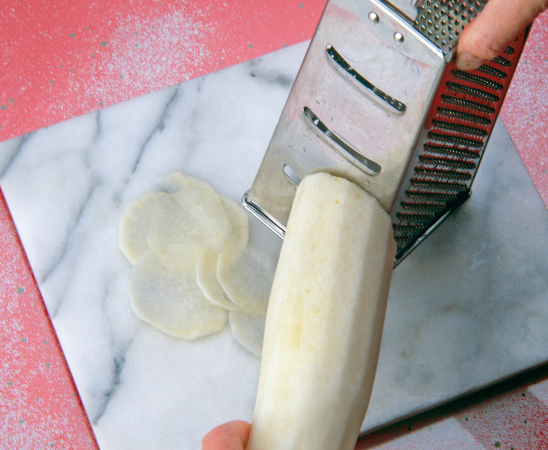 Peeled radish being sliced on grater