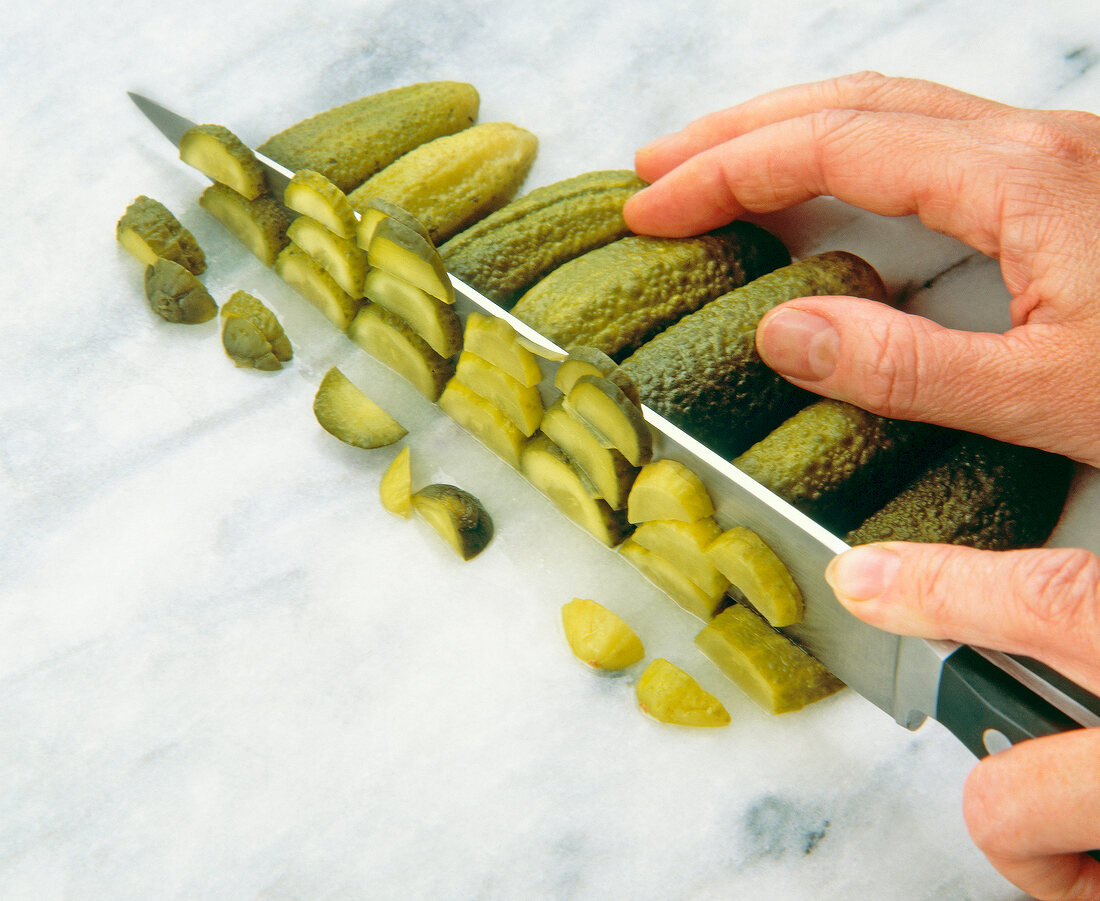Close-up of pickled cucumbers being cut on cutting board with knife