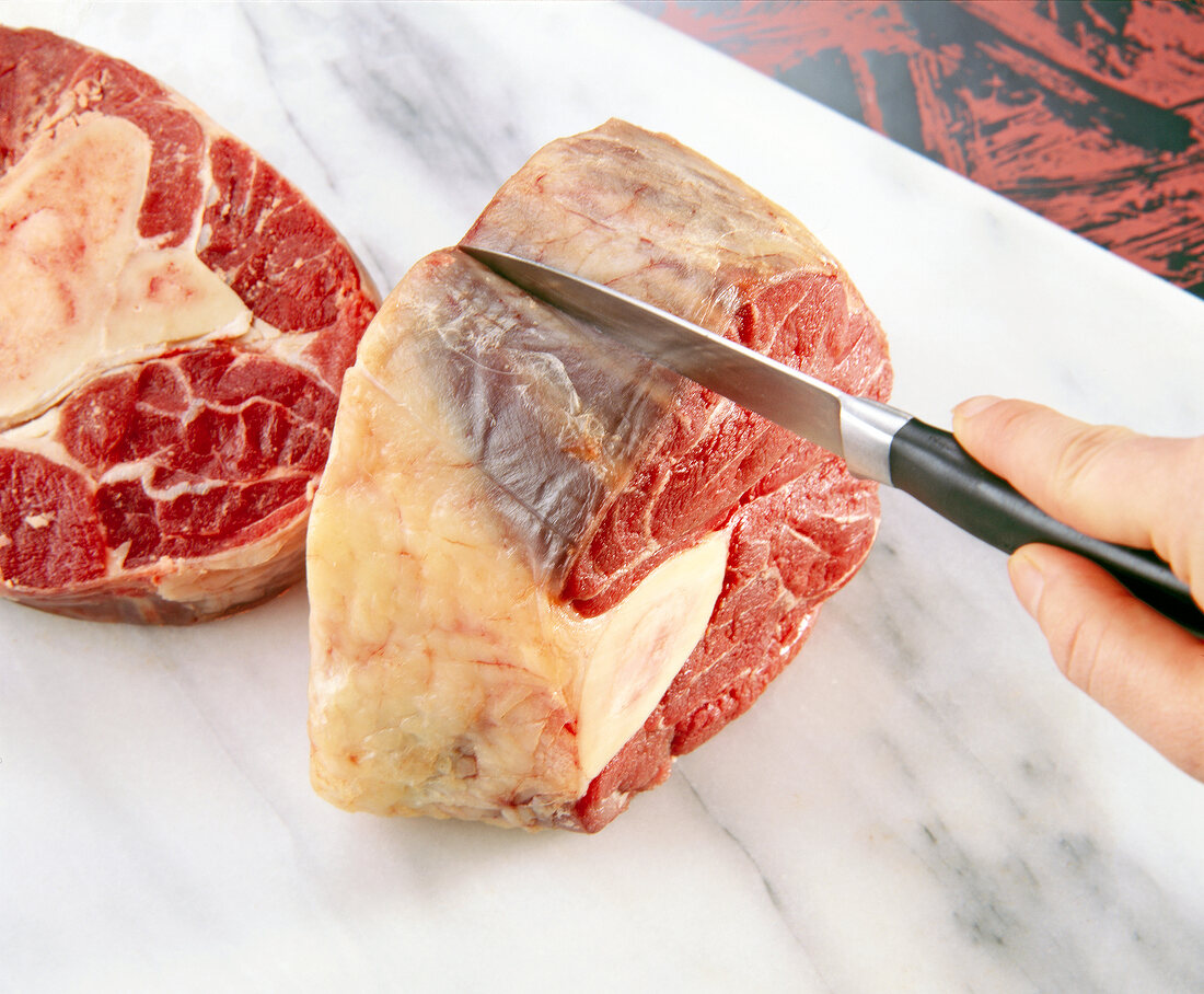 Raw bovine bone being cut in slices with knife on cutting board