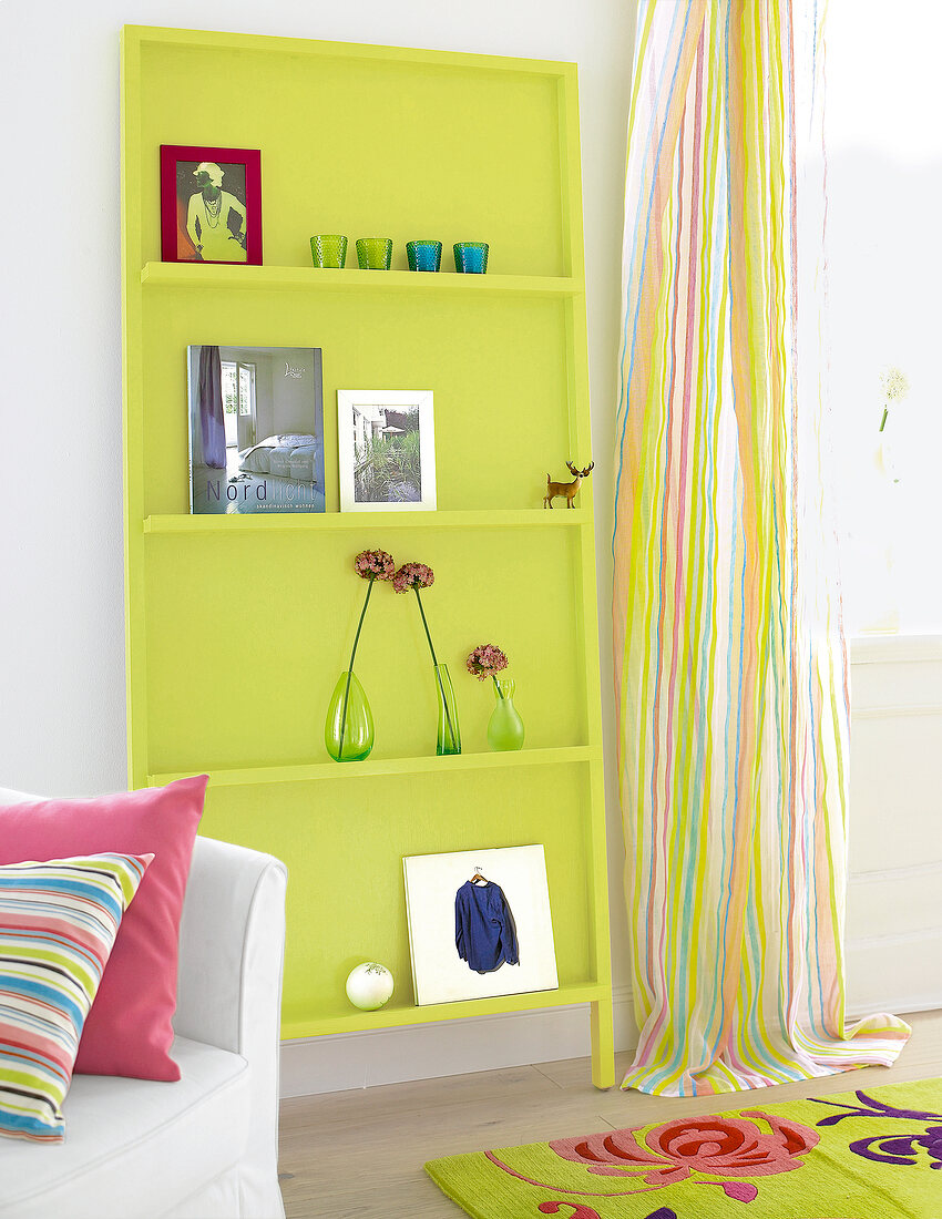 Green leaning bookshelf with books beside striped curtains