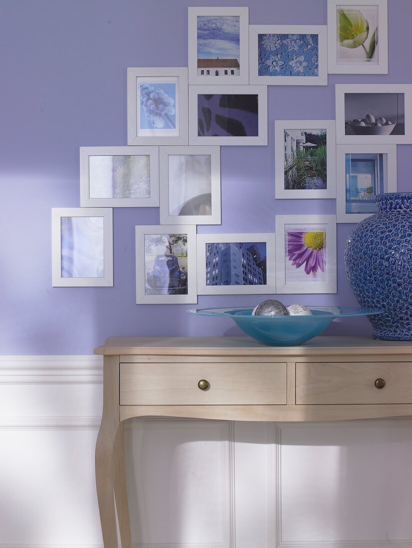 Bilder in kleinen Rahmen an einer hellblauen Wand mit Schubladentisch
