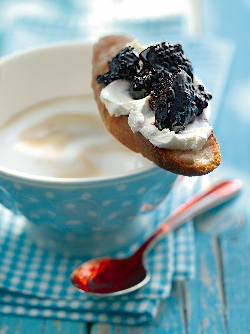 Close-up of jam applied on quark bread and kept on cup of milk coffee