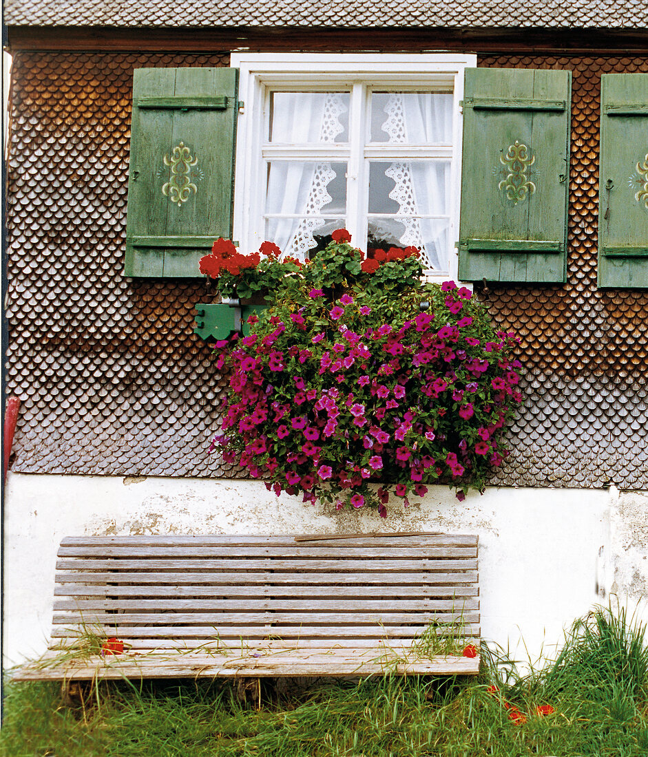 Bank vor einem Bauernhaus mit prachtvollen Blumen vor den Fenstern