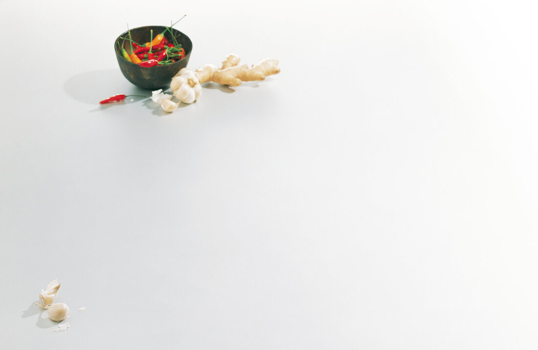 Garlic, ginger tuber and chilli peppers in bowl on white background