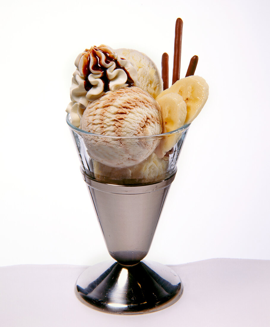 Scoops of ice cream with banana, cream and chocolate sticks in ice-cream glass