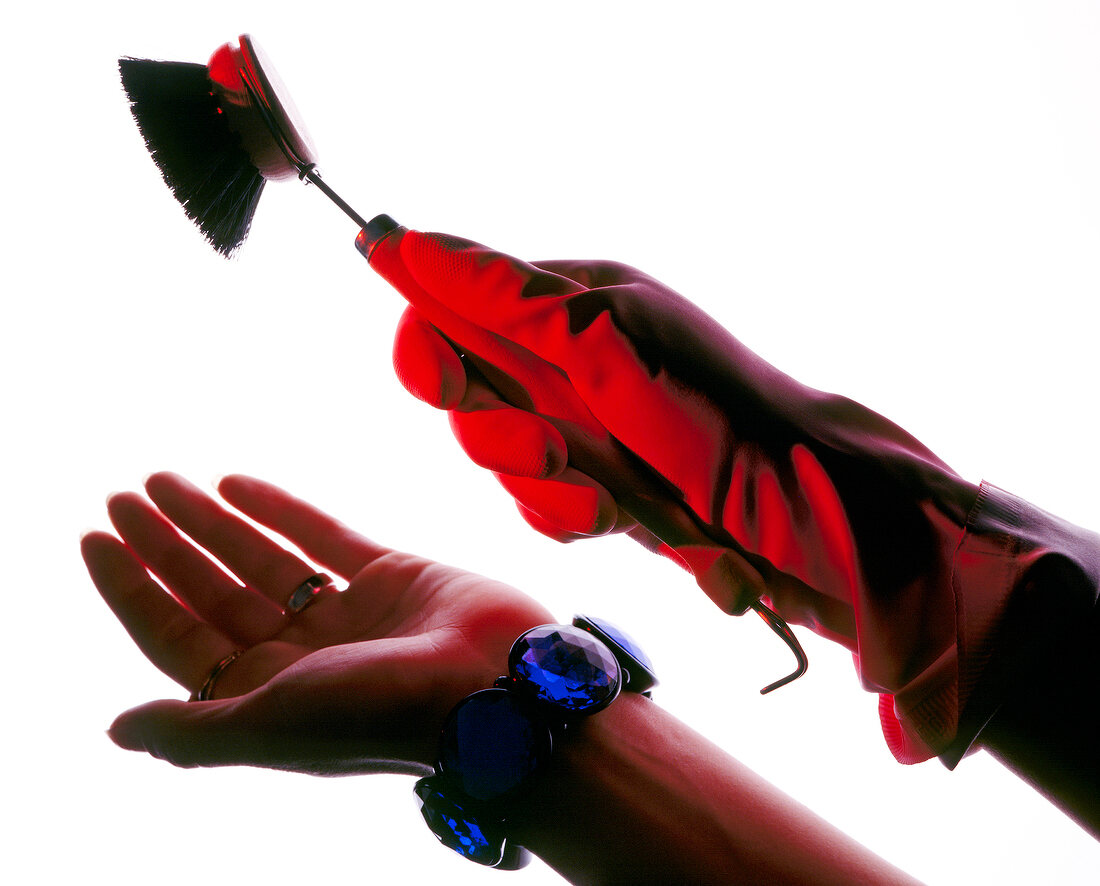 Close-up of woman's hand wearing red gloves and blue bracelets holding small brush