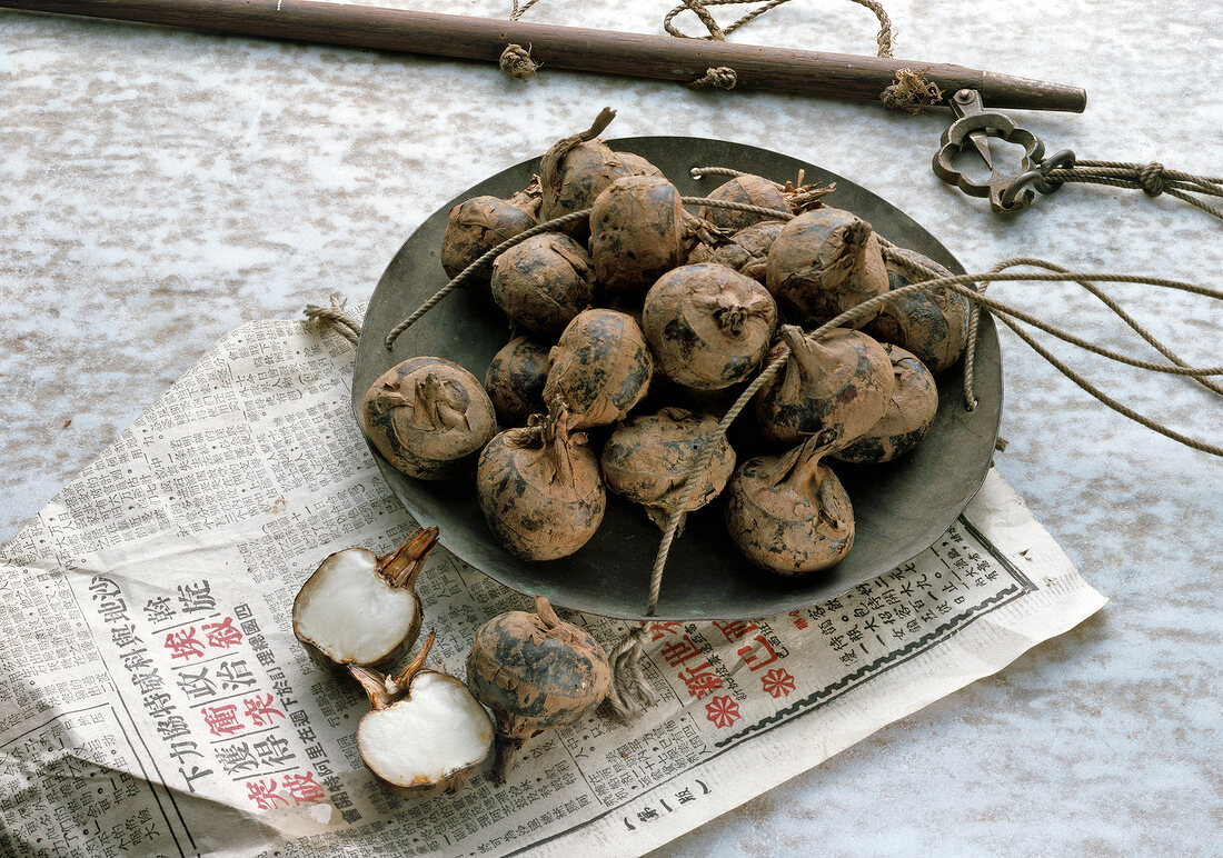 Whole and halved water chestnuts in bowl and on paper