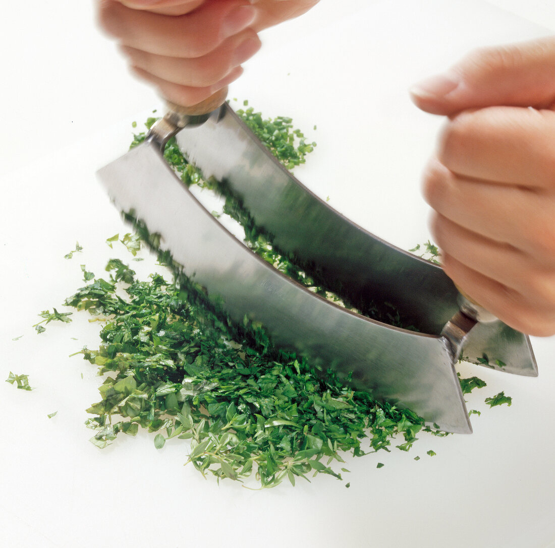 Washed and dried herbs being cut with mezzaluna for preparation of herb butter, step 3