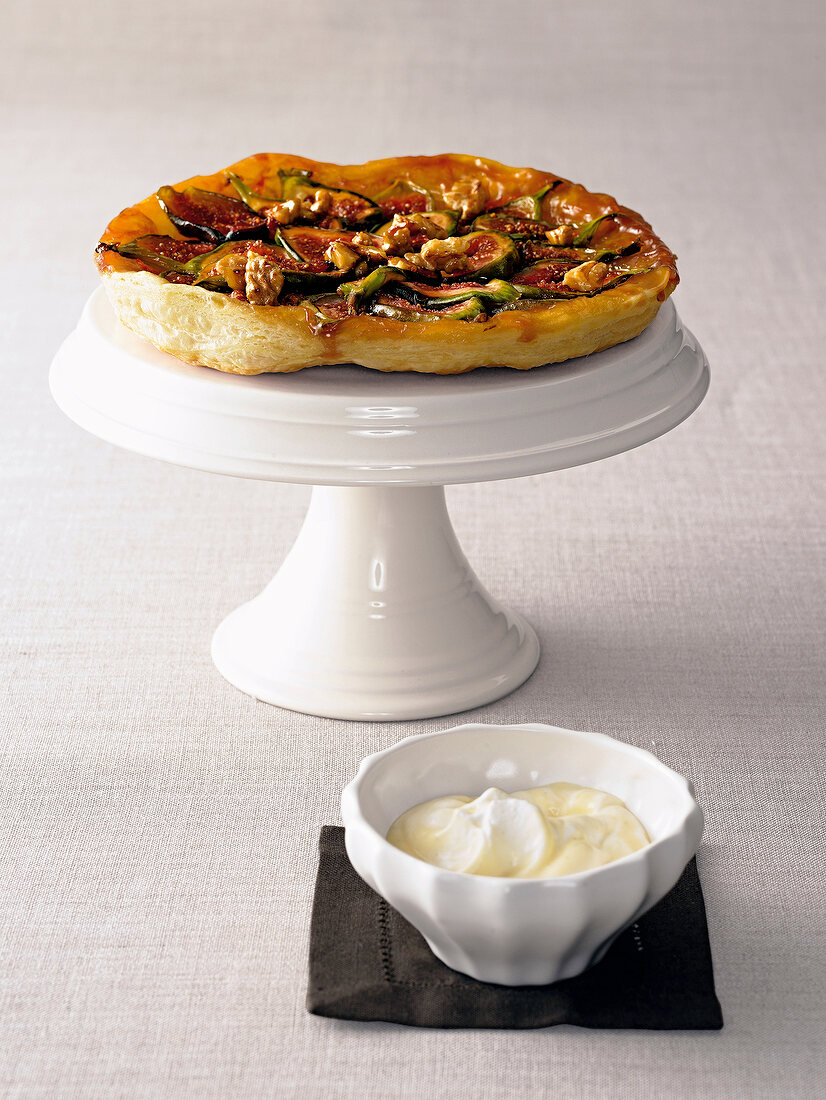 Fig and walnut tart on cake stand served with bowl of vanilla cream