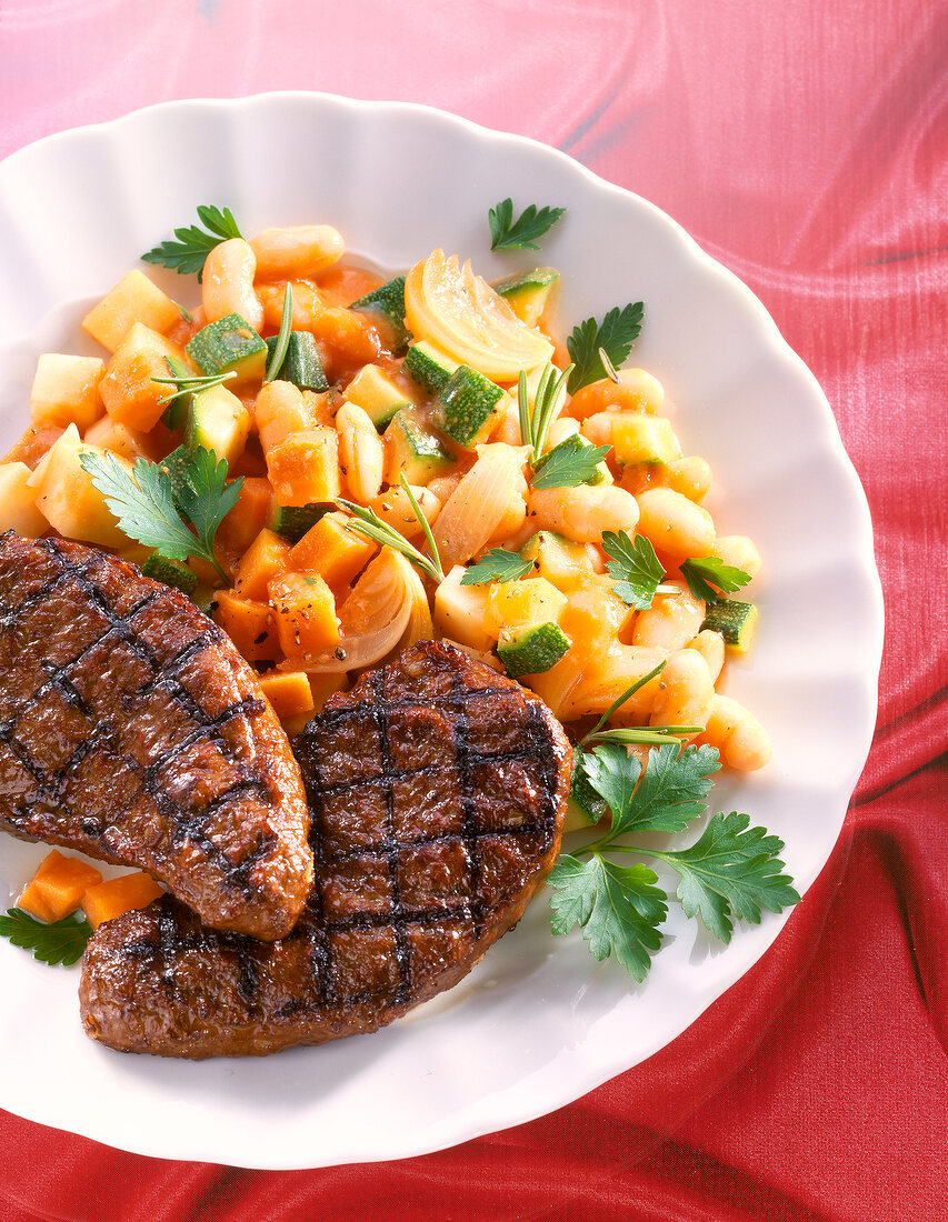 Close-up of steaklets with beans, zucchini, carrots and rosemary in dish