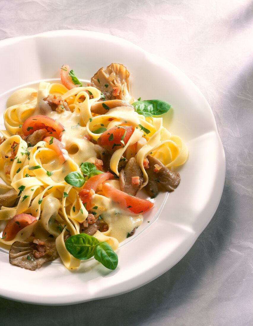 Close-up of fettuccine pasta with oyster mushrooms, tomatoes and bacon in bowl