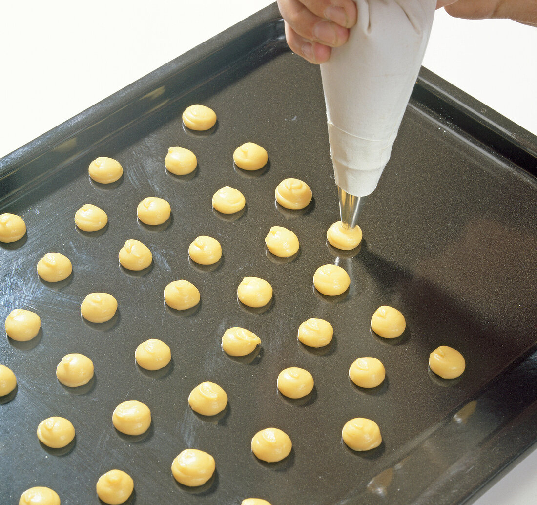 Dabbing fire mass on baking tray with piping bag for preparation of profiteroles, step 1