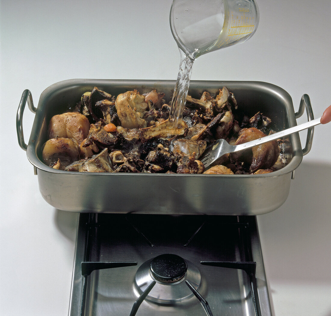 Pouring water to vegetables with roasted bones and veal feet in baking dish, step 4