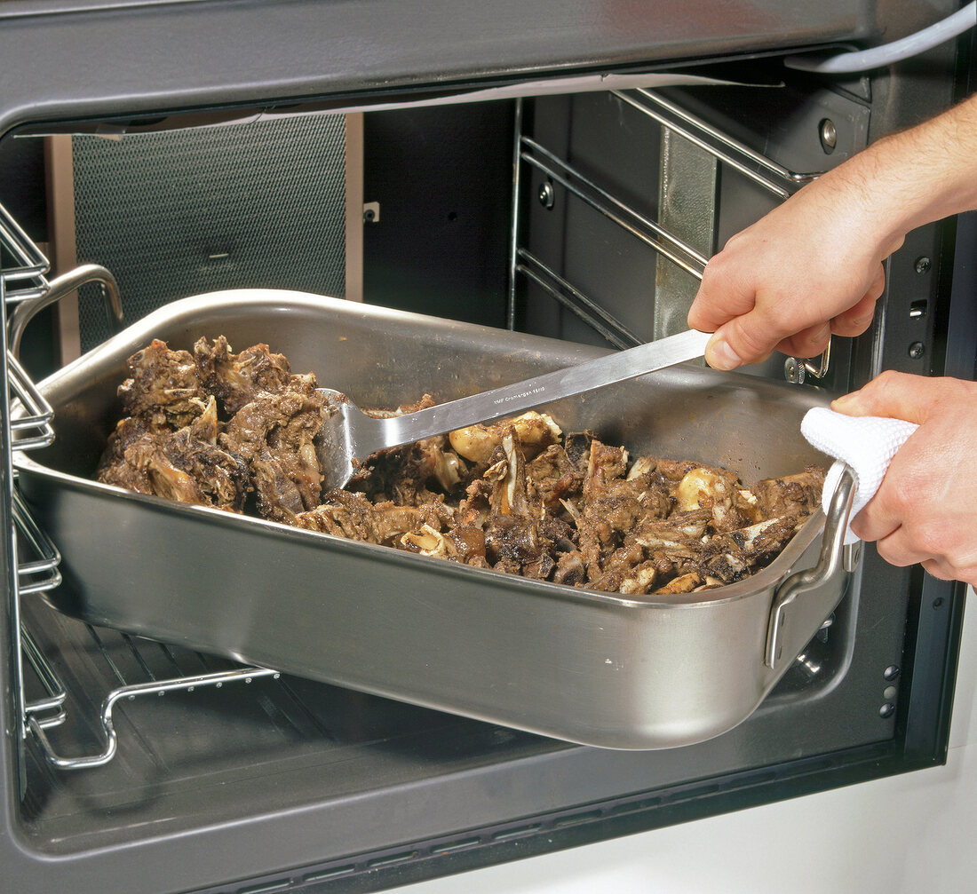 Hand taking out roasting dish with roasted bones in oven, step 2