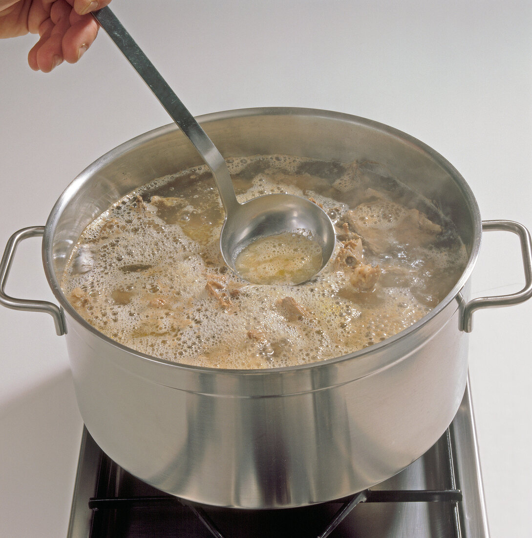 Skimming foam from chicken stock with ladle in pan, step 6