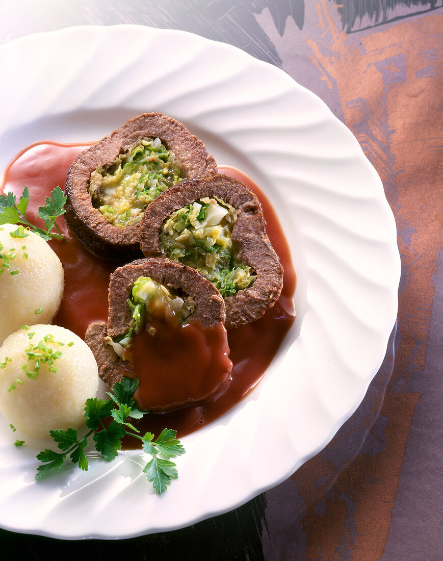 Close-up of stuffed beef with sauce, potato dumplings and parsley on plate