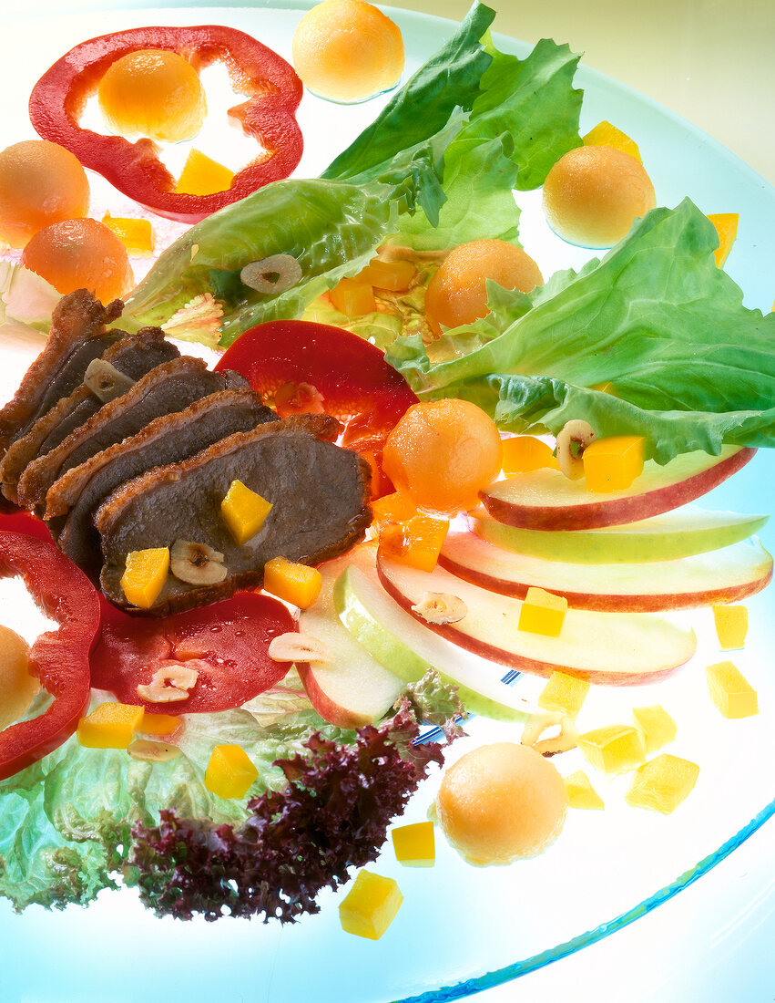 Close-up of duck breast with melon and apple on plate