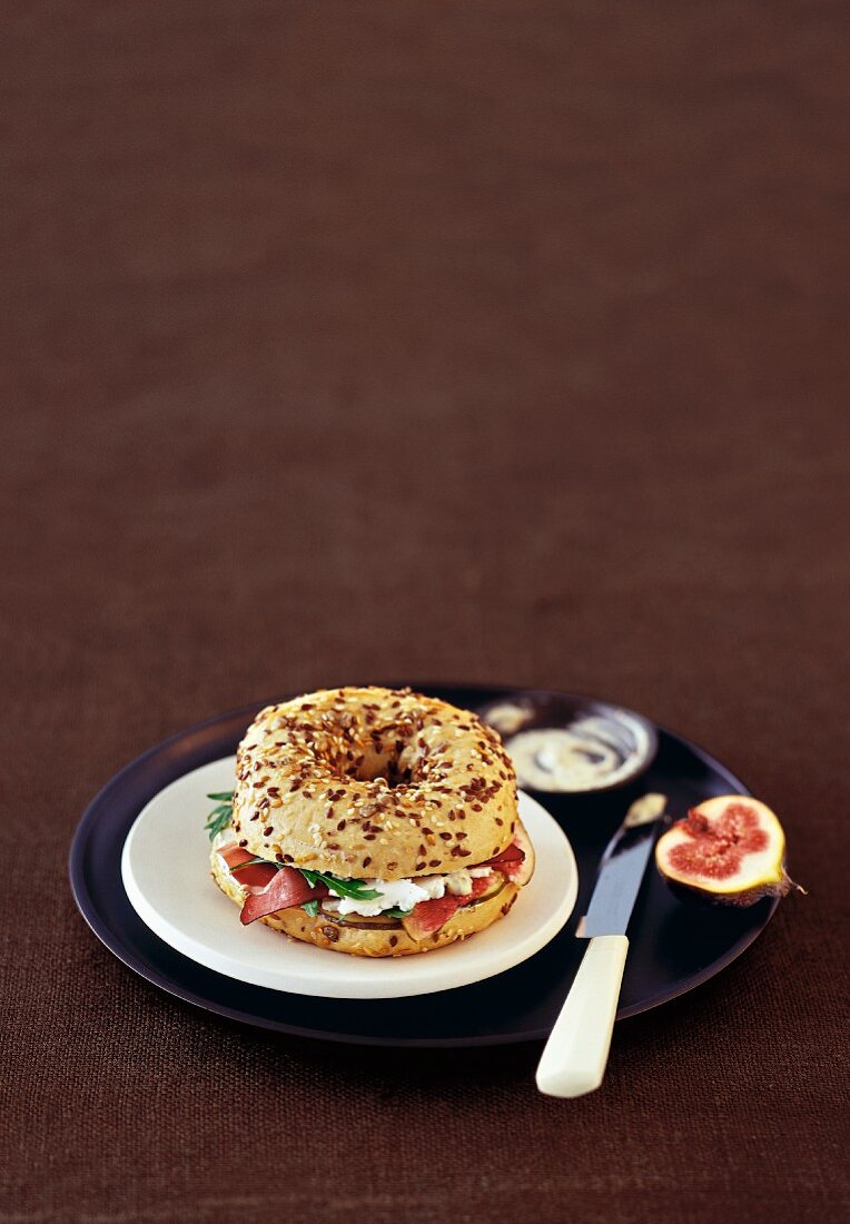 A ham and feta bagel served with figs on a brown plate