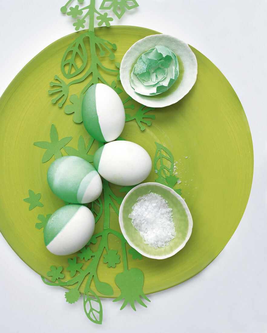 Four half coloured Easter eggs and broken green bowl on green plate