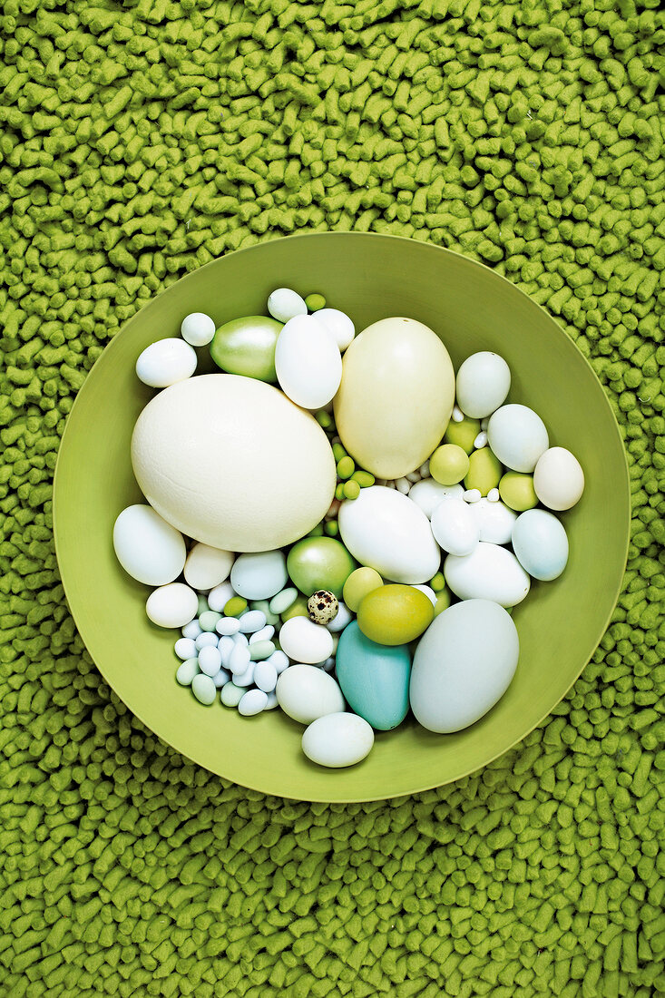 Green bowl of several Easter eggs on green carpet