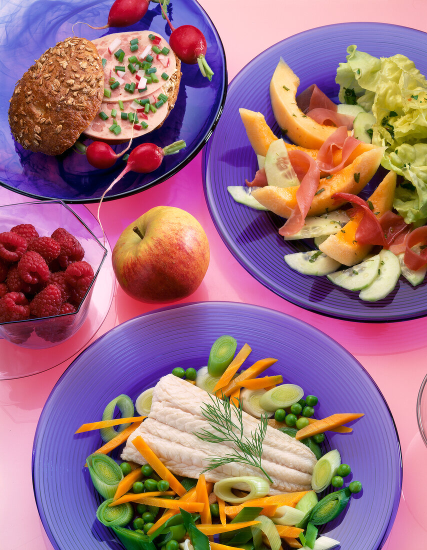 Sandwich, salad, fish fillet with vegetables, apple and berries in plates