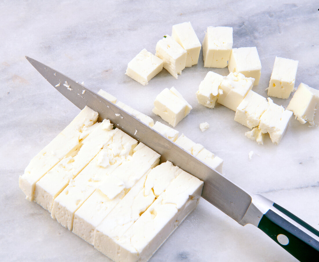 Cutting feta cheese into cubes with kitchen knife