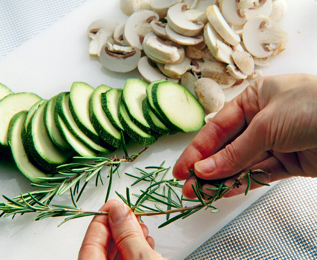 Sliced zucchini and mushrooms on chopping board and rosemary on side