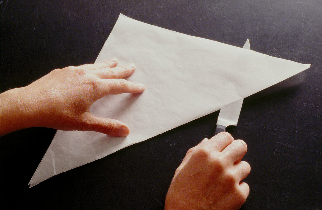 Baking paper being folded in triangular shape and cut into half with knife, step 1