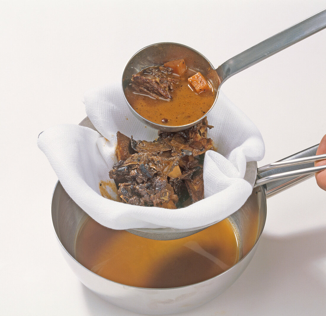 Sauce being strained through cloth strainer in pan, step 7