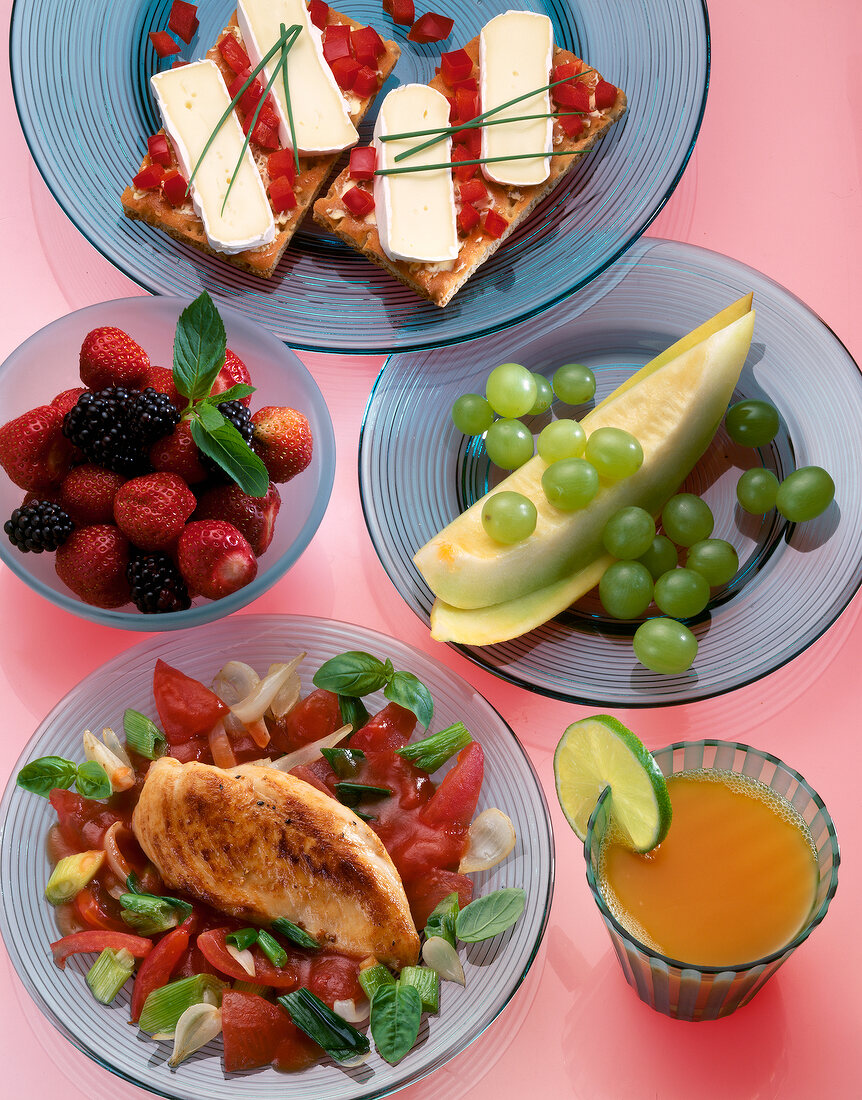 Chicken fillet with vegetables, orange juice, melon, berries and crisp bread on plate
