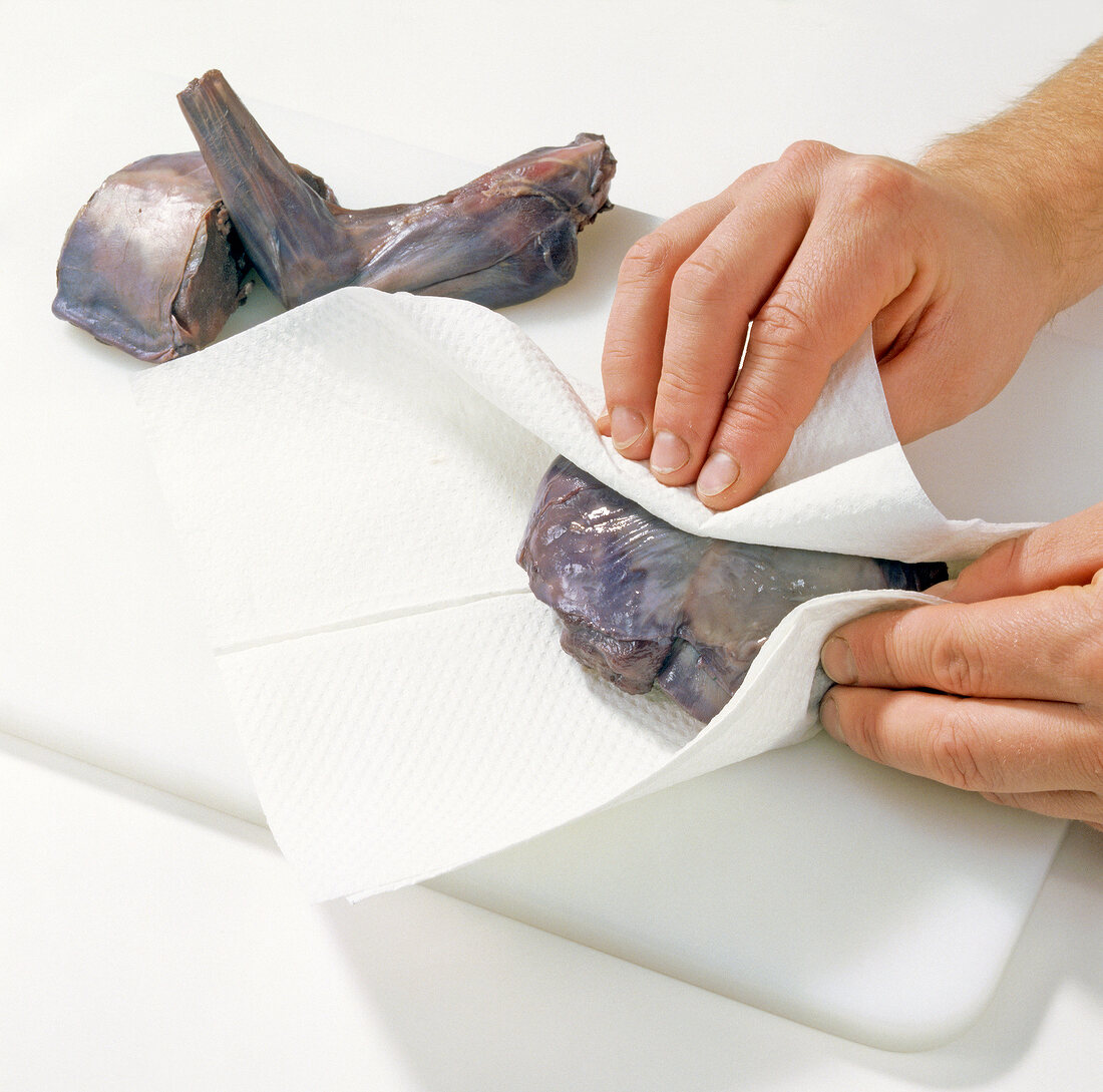 Close-up of hands wrapping rabbit meat in tissue for preparation of hasenpfeffer, step 3