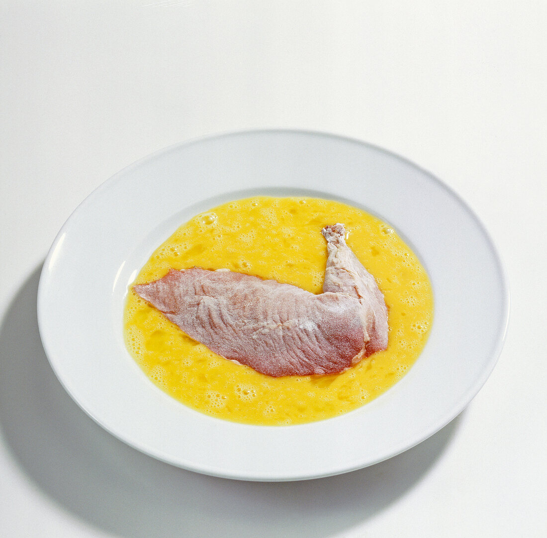 Raw duck leg in egg yolk on plate, step 2