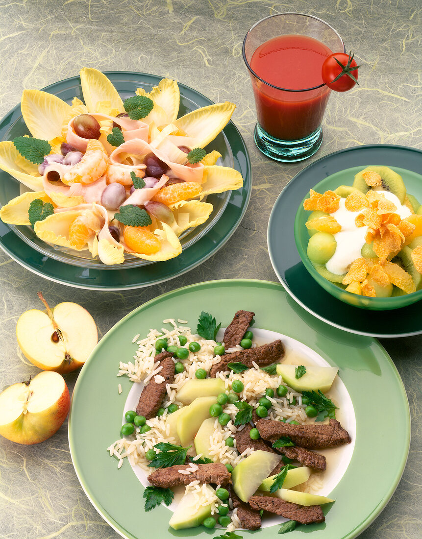 Fruit salad, salad, fried rice with beef on plates with tomato juice and apple