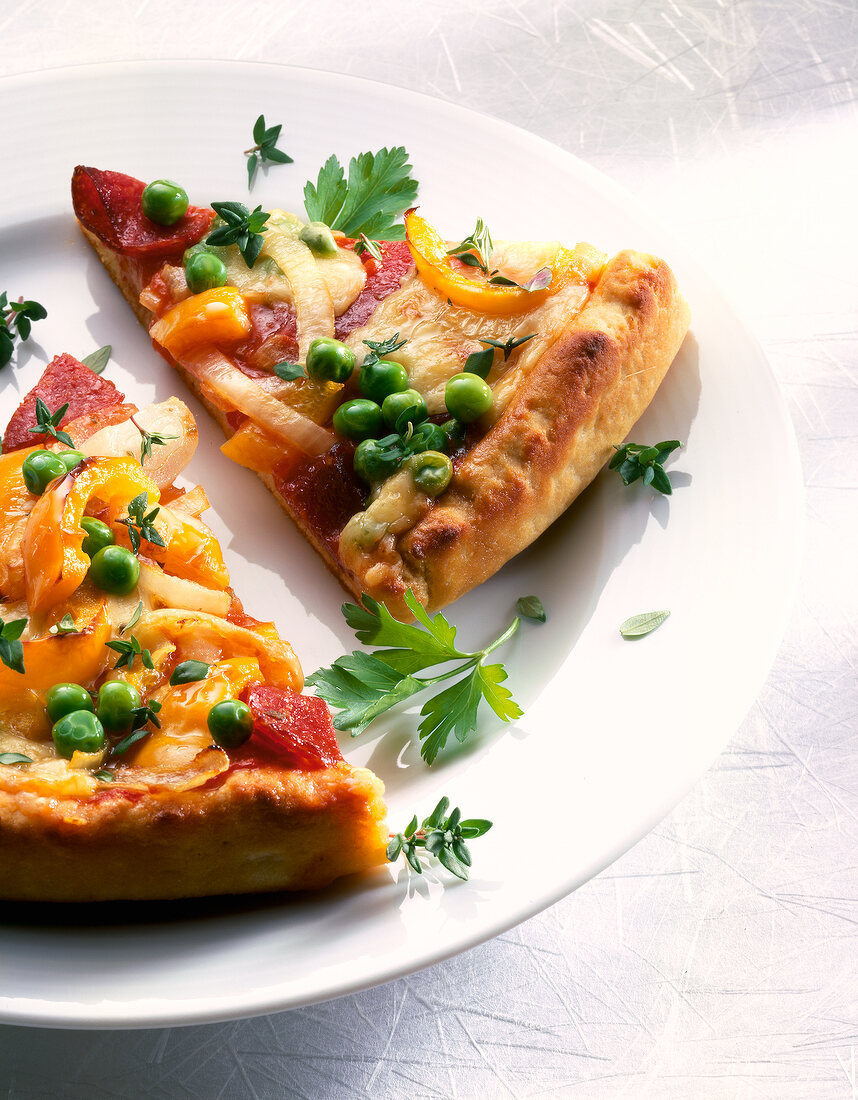 Close-up of slices of potato pizza with salami, peas and parsley on plate