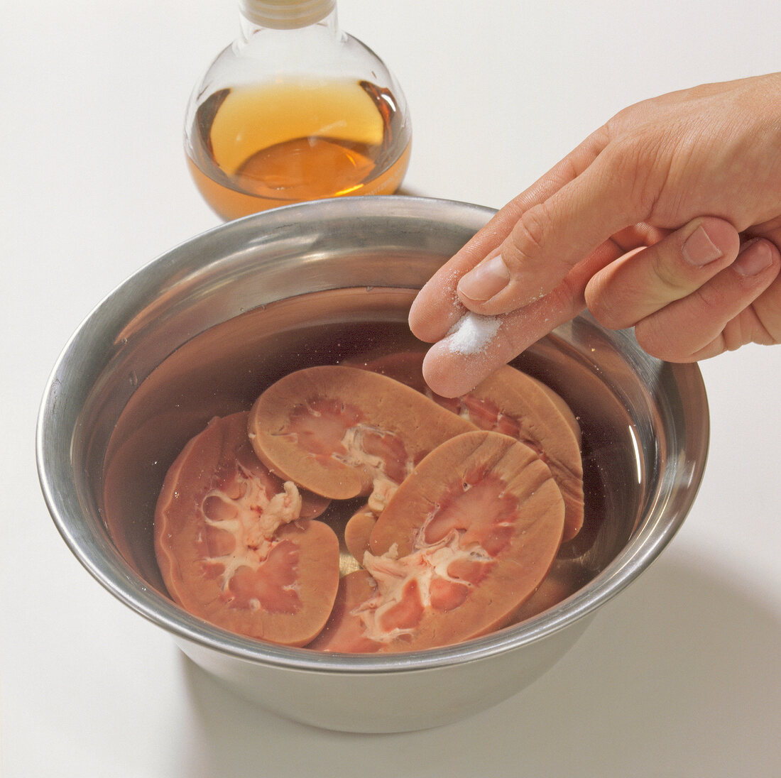 Close-up of hand adding salt in water with wild boar kidneys, step1