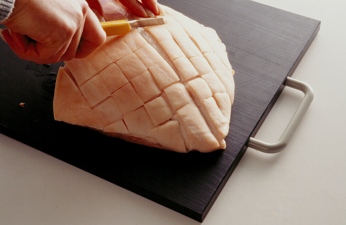 Roasted pork being carved diagonally with knife on wooden board, step 1