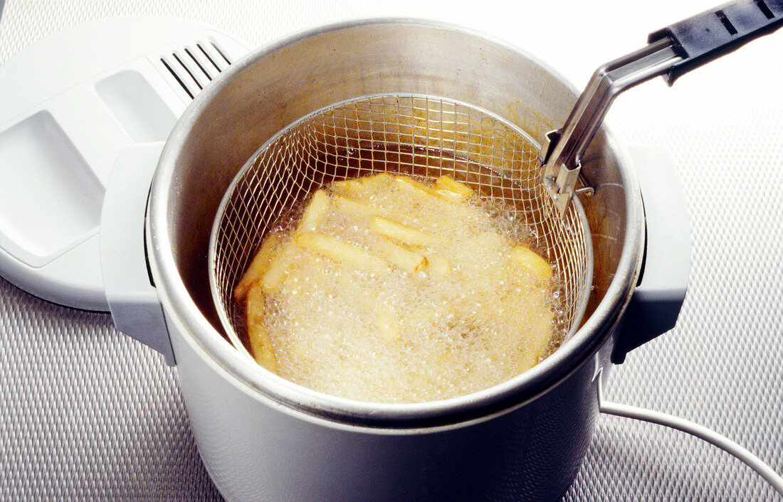 Pommes werden in der Friteuse fritiert, close-up.