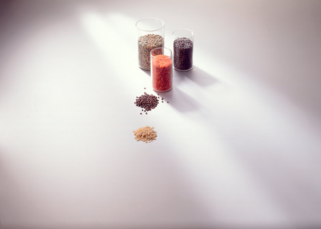 Different types of lentils in glass container on white background