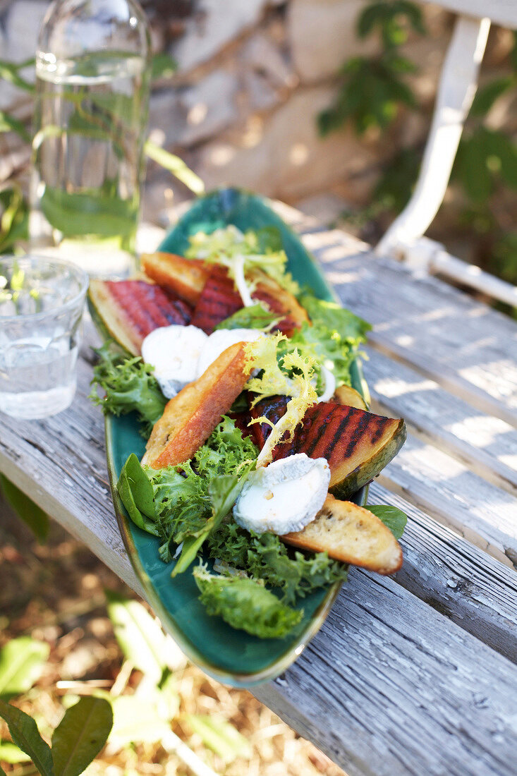 Salat mit gebratener Melone in einer Schale auf einem Holztisch