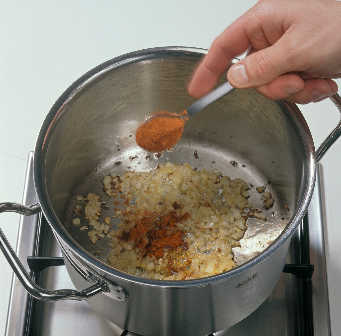 Close-up of sprinkling paprika powder on onions while preparing goulash soup, step 2