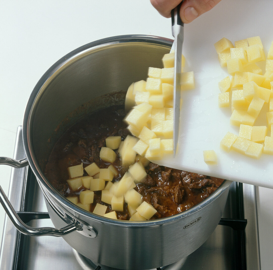 Close-up of adding potato cubes to meat and onions while preparing goulash soup, step 6