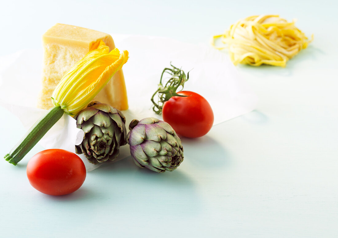 Two artichokes, tomatoes and piece of cheese on white background