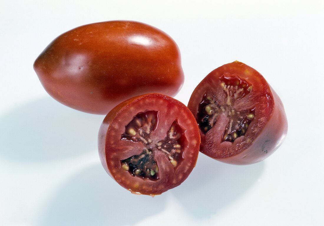 Whole and halved red long plum tomatoes on white background