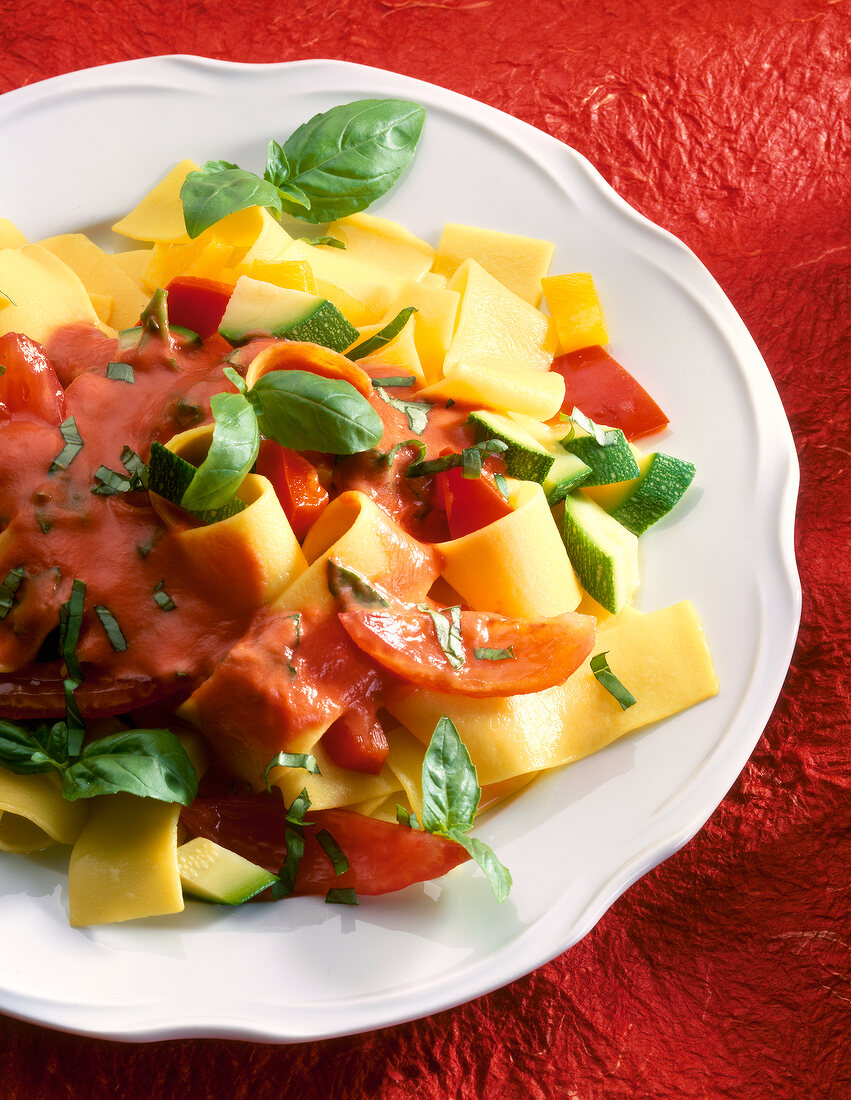 Nudeln mit Paprika-Tomaten-Sauce auf Teller, Basilikumblättchen