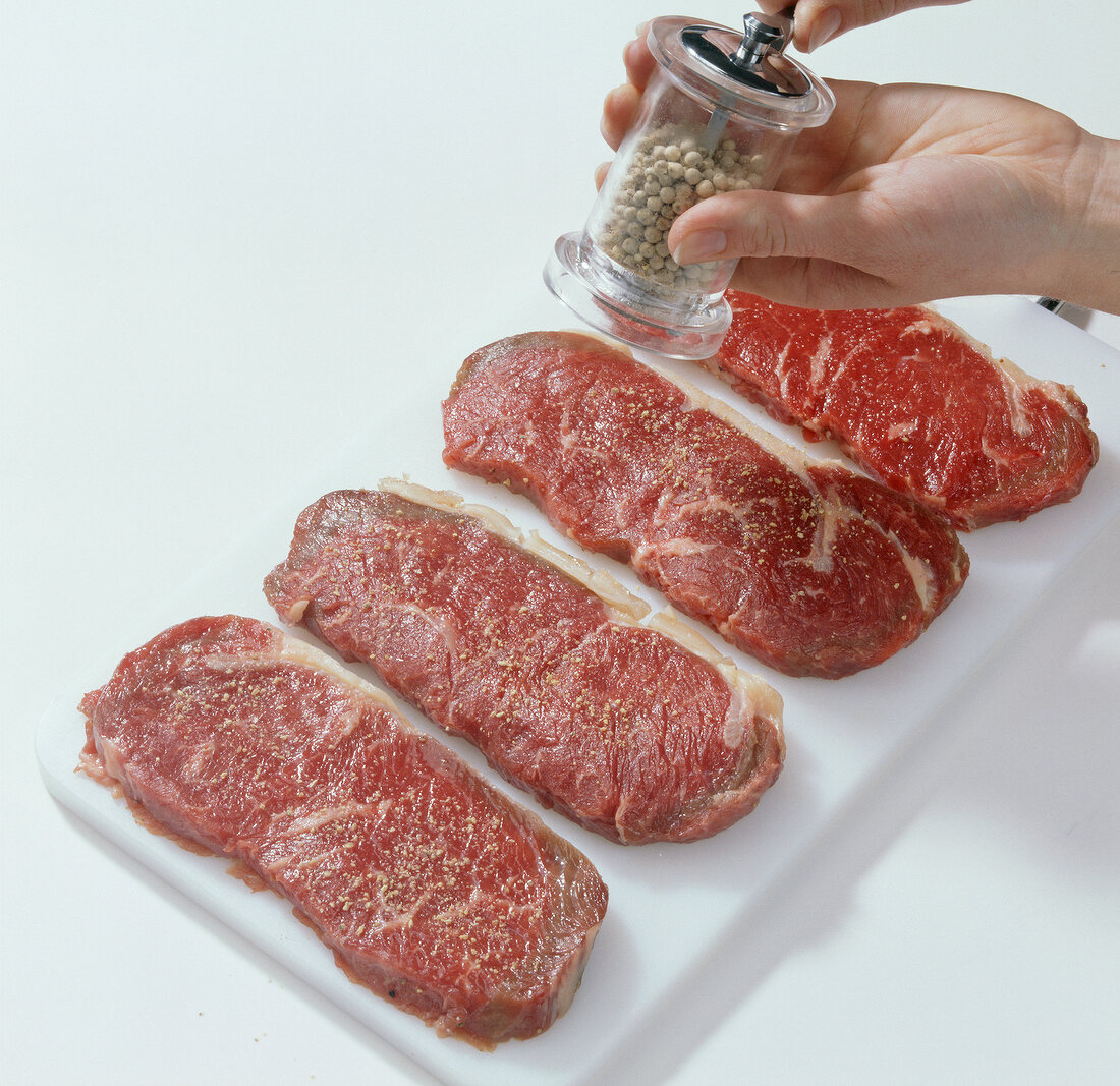 Close-up of sprinkling pepper spices on roasted pieces of beef, step 1