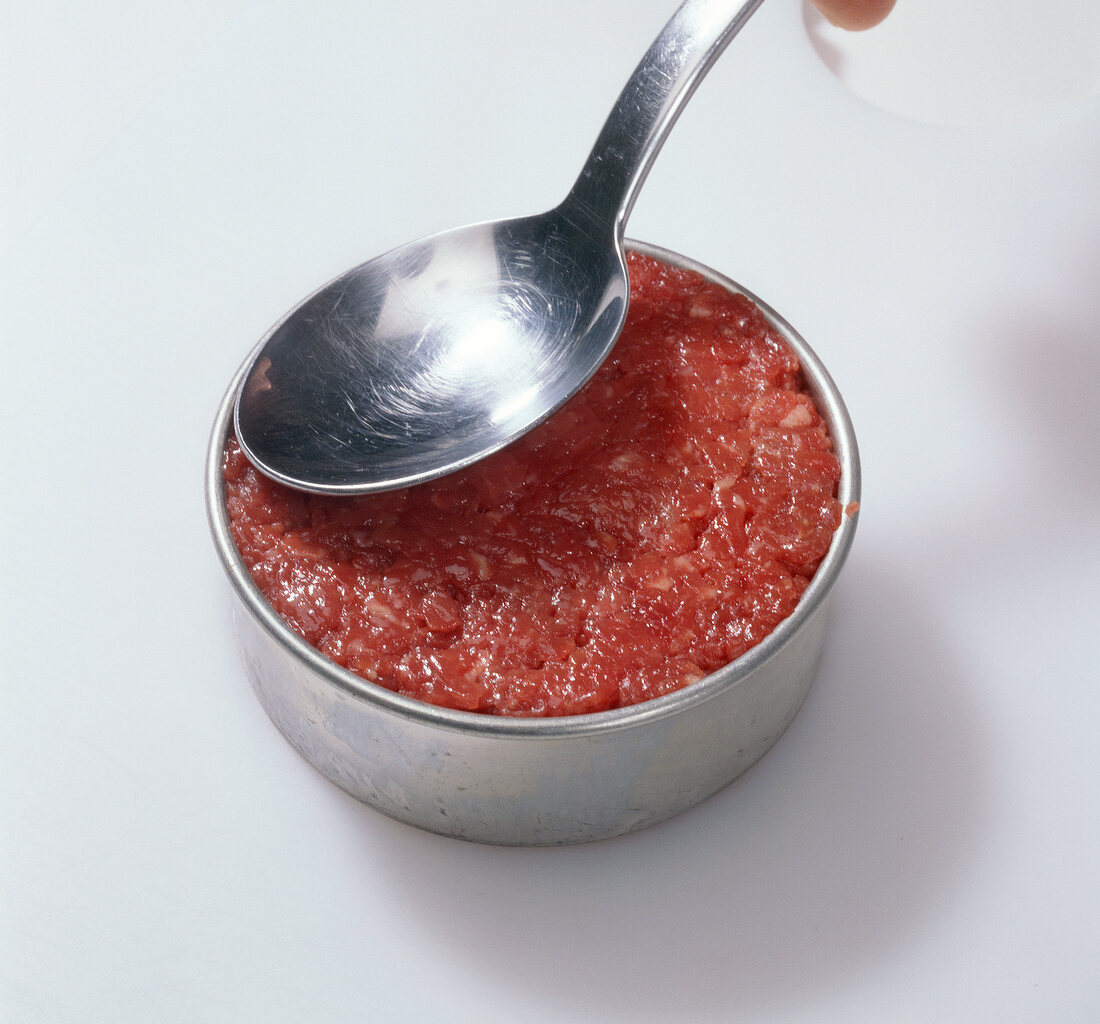 Close-up of filling beef into cup while preparing hamburgers, step 4