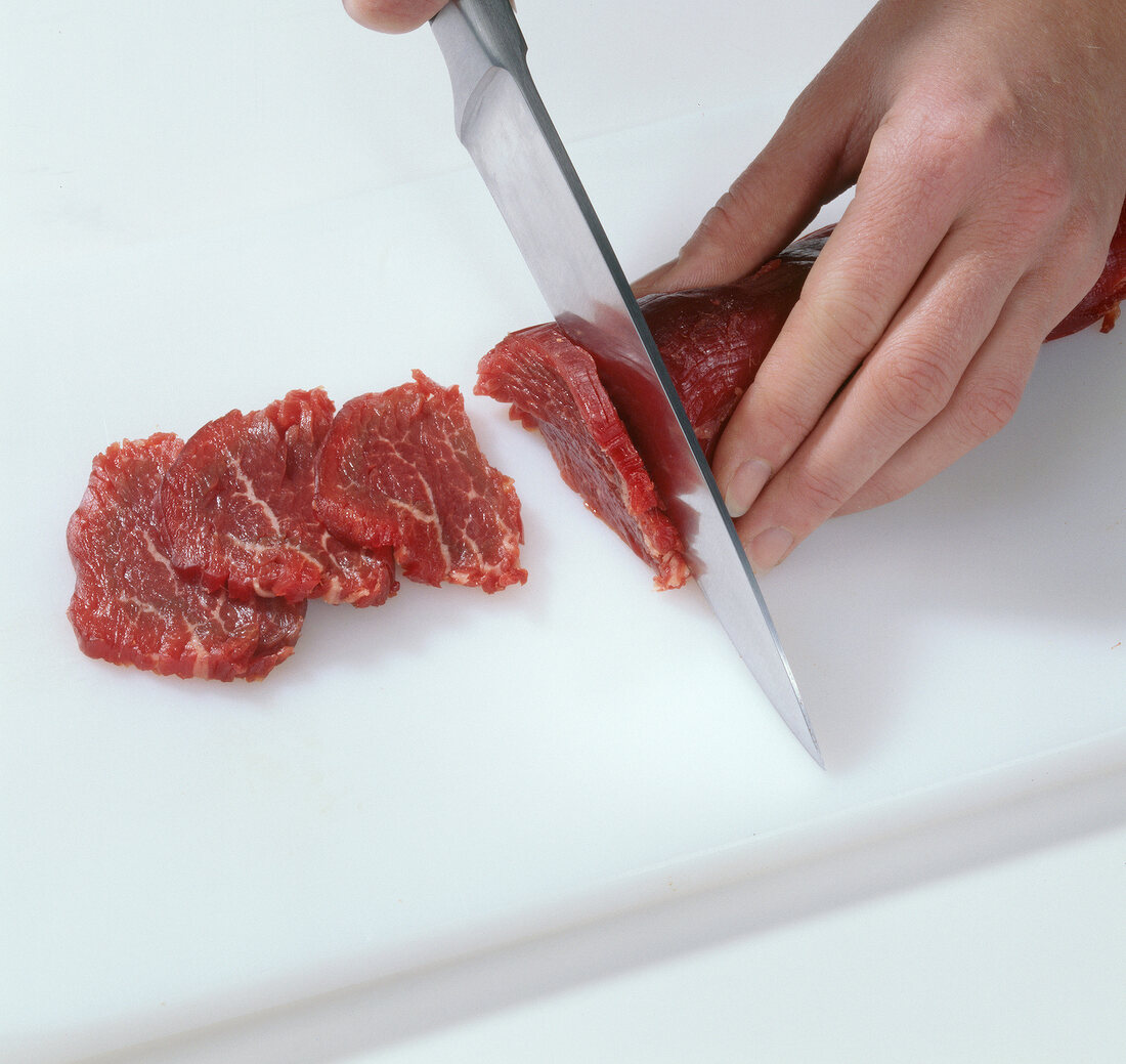 Close-up of hands cutting beef in slices for preparing hamburgers, step 2