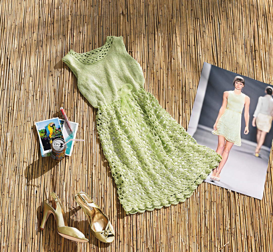 Green crochet summer dress, sandals and photographs lying on bamboo mat