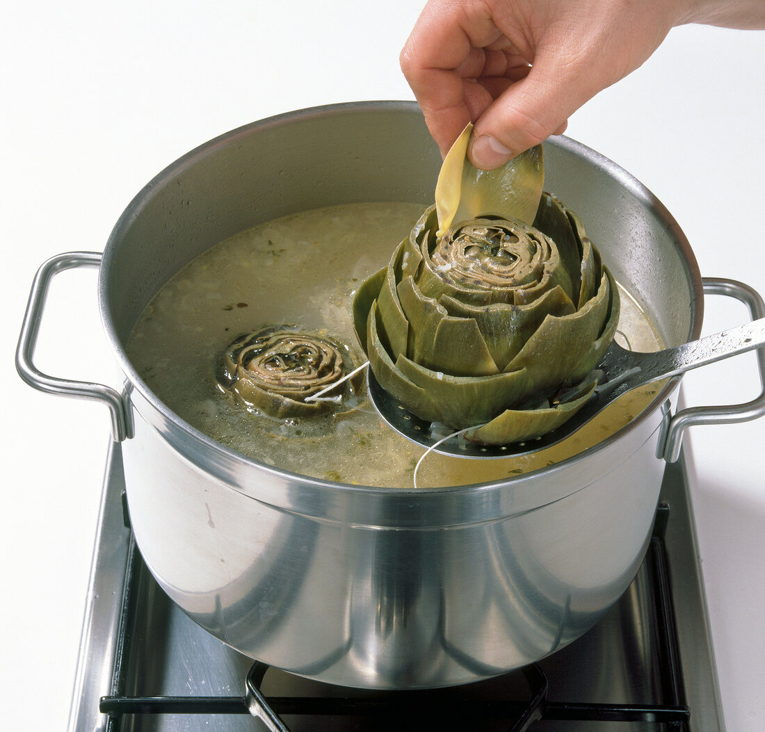 Close-up of leaf being removed from boiled artichoke over pot of boiling water, step 10