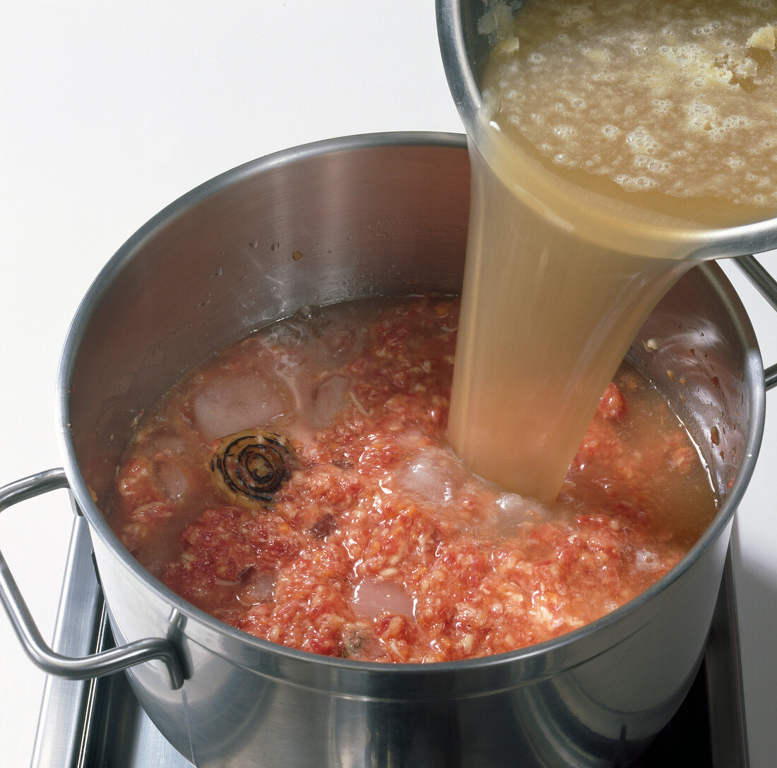 Pouring beef broth in pot with meat, siler root and ice cubes